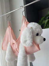 Pink mesh dog harness on pet grooming hammock for nail trimming with fluffy poodle toy