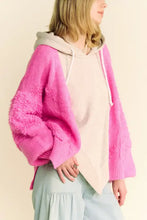 Woman in pink long sleeve cardigan with hood, beige hoodie, and wide light blue pants