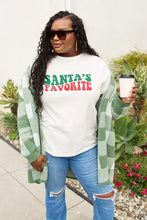 Plus-size woman in Santa’s Favorite round neck t-shirt, green plaid cardigan, and ripped blue jeans, holding coffee cup