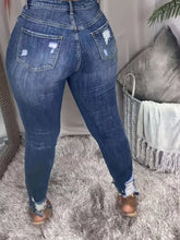 Plus size slim fit distressed jeans in high-waisted blue denim with distressed pockets and frayed cuffs
