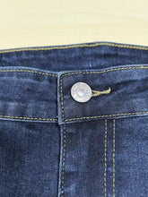 A silver circular button engraved on dark blue denim fabric of plus size slim fit distressed jeans
