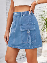 Blue denim pocketed buttoned denim skirt mini length with large front pocket secured by metal buckle and drawstring