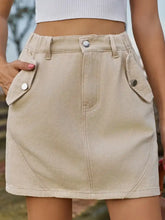 Beige mini denim skirt with buttoned flap pockets and fitted waistband in durable denim fabric