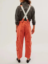 Person in pocketed wide strap denim overalls with orange pants and suspenders