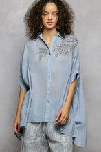 Light blue pol button down high low hem shirt with loose fit and delicate silver leaf embroidery across the chest