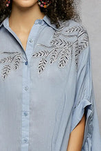 Light blue pol button high low hem shirt with intricate silver leaf embroidery on shoulders for elegant wear