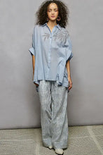 Light blue pol button high low hem shirt with delicate silver leaf embroidery on the chest