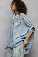Light blue pol button loose-fitting shirt with intricate silver embroidery and high low hem detailing on chest