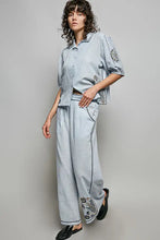 Light blue denim-like lightweight woven two-piece outfit with embroidered floral details on sleeves and pant legs