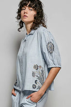 Light blue lightweight woven linen blouse with embroidered floral black detailing on sleeves and front in short sleeve style