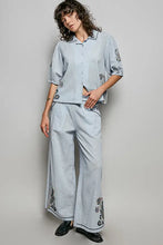 Light blue lightweight woven linen pants with embroidered floral black patterns along sides and hem complementing pol shirt