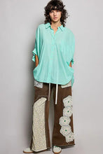 A woman wearing a mint-green pol button down half dolman sleeve shirt paired with wide-leg brown trousers with lace appliqués