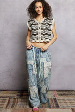 A woman wearing a black and cream pol crochet button vest with scalloped edges and a crochet crop top design