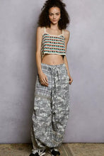 A woman wearing a pol cropped crochet cami with scalloped edge and patterned wide-leg newspaper print pants