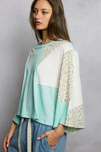 A soft mint green and white textured slub knit round neck top with floral embroidery on the sleeves