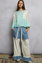 A woman wears a mint green and white textured slub knit round neck top with floral embroidery and patchwork design