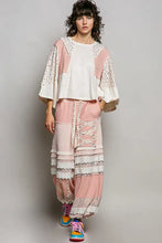 A woman wears a pink and white textured slub knit patchwork round neck top with lace trim and matching ruffled pants