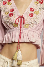 A soft pink cropped blouse with intricate floral embroidery, flared ruffle sleeves, and decorative tassels