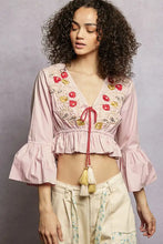 Pink cropped blouse with embroidered red and gold floral patterns and flared ruffle sleeves with tied neckline cord