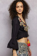 Black floral embroidered cropped blouse with gold and red detailing, flared bell sleeves, and ruffled hem