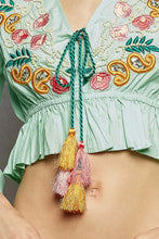 Light green floral embroidered cropped blouse with pink gold white thread, ruffled hem, and colorful tassels front tie