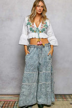 Wide-leg denim pants with faded blue wash and floral embroidered layered patchwork design along the seams
