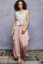A woman wearing a white pol floral embroidered v neck vest with pink floral embroidery and matching patterned harem pants