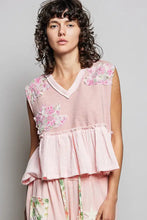 A soft pink sleeveless top featuring floral patch ruffled embroidery on shoulders and a tiered ruffled hem with raw edge detail