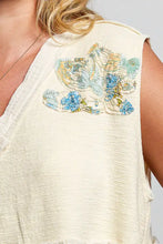 Cream-colored patch ruffled sleeveless top with floral patch appliqué in blue and yellow and raw edge detail