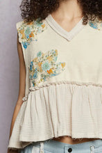 Beige sleeveless top with intricate blue and orange floral patch ruffled embroidery and raw edge detail