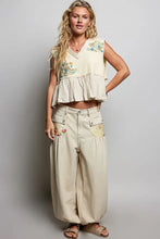Beige floral patch ruffled sleeveless top with raw edge detail and embroidered floral design at the hem