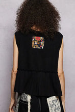 Back view of black sleeveless pol floral patch top with raw edge detail and colorful floral patch on ruffled hem