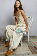 Beige patchwork wide-leg pants with floral and map-patterned fabric paired with pol lace neck ribbed cami