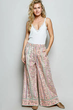 A pair of wide-leg pink patterned pants with floral and striped designs paired with pol lace neck ribbed cami