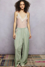 A soft sage green satin wide-leg pant with embroidered side panels and a drawstring waist paired with a pol lace neck ribbed cami tank