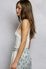 A woman wears a white pol lace detail v-neck ribbed cami paired with light blue floral wide-leg pants