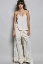 A woman wearing a cream-colored textured knit cami with lace detail v-neck and spaghetti straps