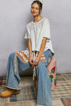 Woman wearing a white embroidered pearl stud short sleeve shirt with round neck and patchwork denim pants