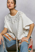 White short sleeve shirt with lace detailing and pearl stud embellishments along the round neck and front panel