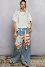 Wide-leg denim pants with white orange and blue patchwork star panels paired with a pearl stud short sleeve shirt