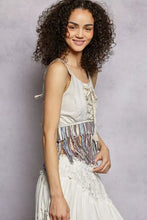 A woman wears a cream pol lace fringe hem tank with lace-up detailing and a colorful woven belt
