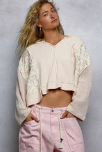 A cream-colored quilted knit cropped sweater with ribbed texture, raw edge detail, and floral pattern sleeves