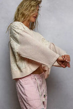 Cream-colored cropped hoodie with quilted knit waffle texture, raw edge details, and floral pattern embroidery on sleeves
