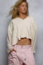 A cream-colored quilted knit cropped sweater with raw edge and floral pattern sleeves featuring ribbed texture