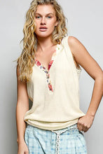 Cream-colored ribbed knit sleeveless tank with contrast floral neckband and button placket detail