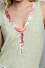 A light green ribbed knit sleeveless top with a contrast floral neckband and button placket for casual wear