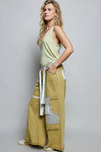 Olive green wide-leg pants with white and striped denim patchwork tied at the waist, paired with pol ribbed v-neck tank with contrast floral neckband