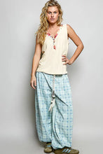 A woman wearing a cream ribbed v neck tank with contrast floral neckband and button details on sleeveless top