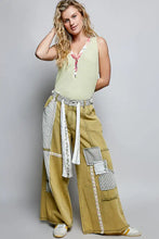 A pair of wide-leg olive-green denim pants with patchwork design paired with a pol ribbed v-neck tank with contrast floral neckband