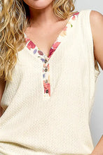 Cream-colored ribbed knit sleeveless tank with contrast floral neckband and v-neck button placket